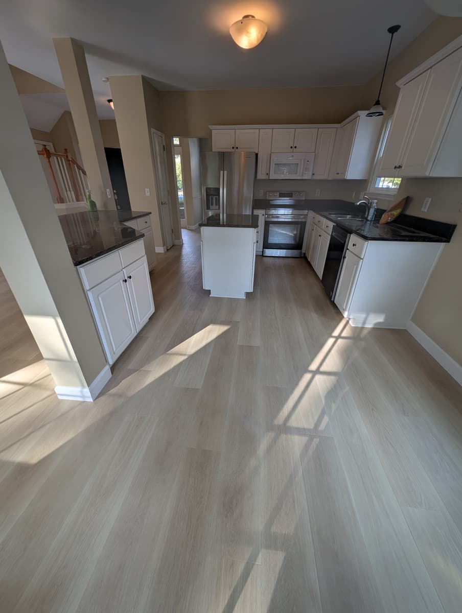 Light luxury vinyl plank through a white kitchen, with sunlight across the floor