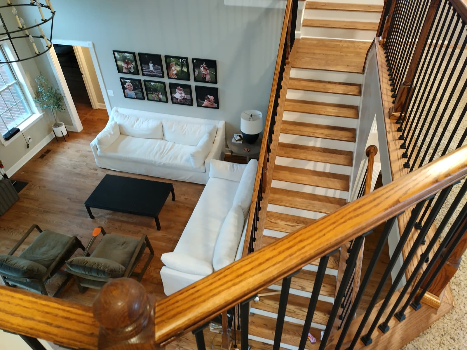Looking down a stained oak staircase with black iron balusters onto a bright living room, built by Forever Flooring