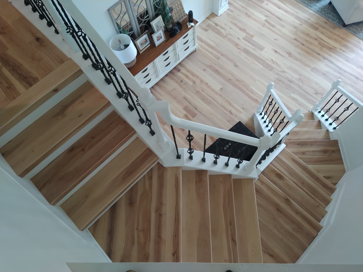 A winding oak staircase seen from above, with white newels and iron balusters
