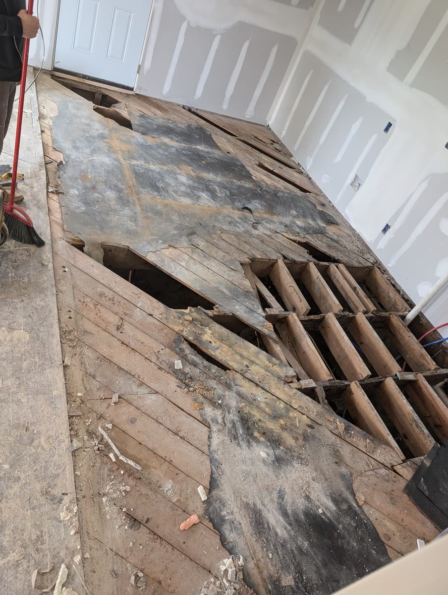 Rotted subfloor boards torn up to expose the joists beneath